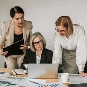 Three women are looking at a laptop in front of them.