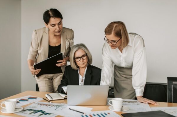 Three women are looking at a laptop in front of them.