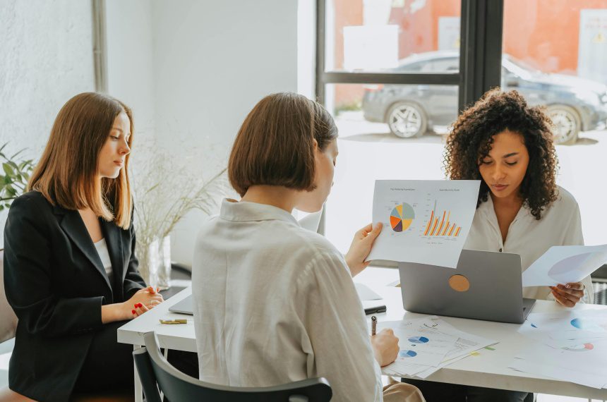 Three women are sitting at a table with papers.